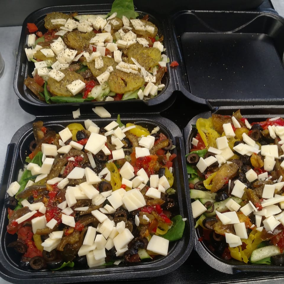 Three takeout containers hold colorful salads topped with sliced vegetables, black olives, and shredded white cheese.